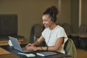 African American woman in a call center setting, working on a laptop and wearing a headset.